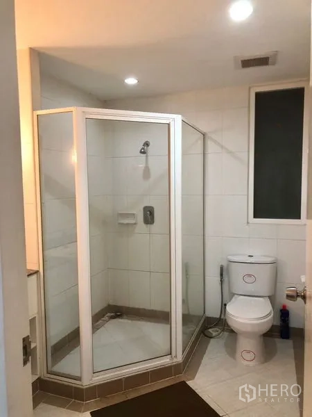 Condominium for rent or sale in Watthana, Bangkok - Modern bathroom with glass-enclosed shower, toilet, and tiled walls.