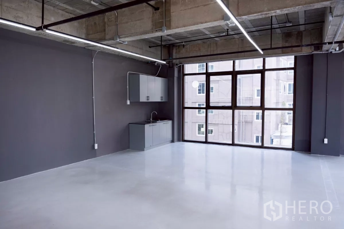 Office Space for rent - Open-plan Bangkok office with kitchenette, floor-to-ceiling windows, exposed ceiling and LED strip lights.