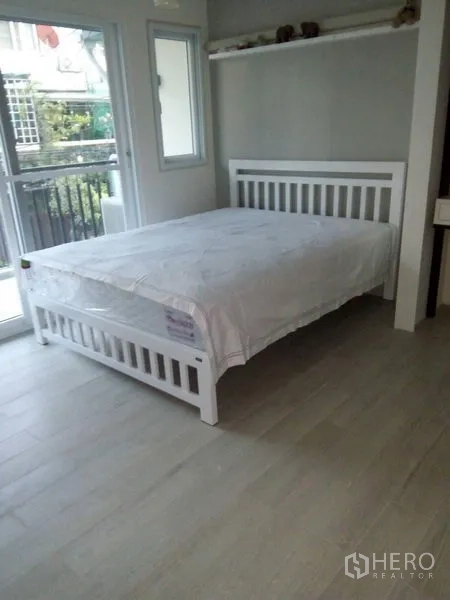 Townhouse for sale in Khlong Toei, Bangkok - Second bedroom with balcony doors, corner windows, and pale wood floors.