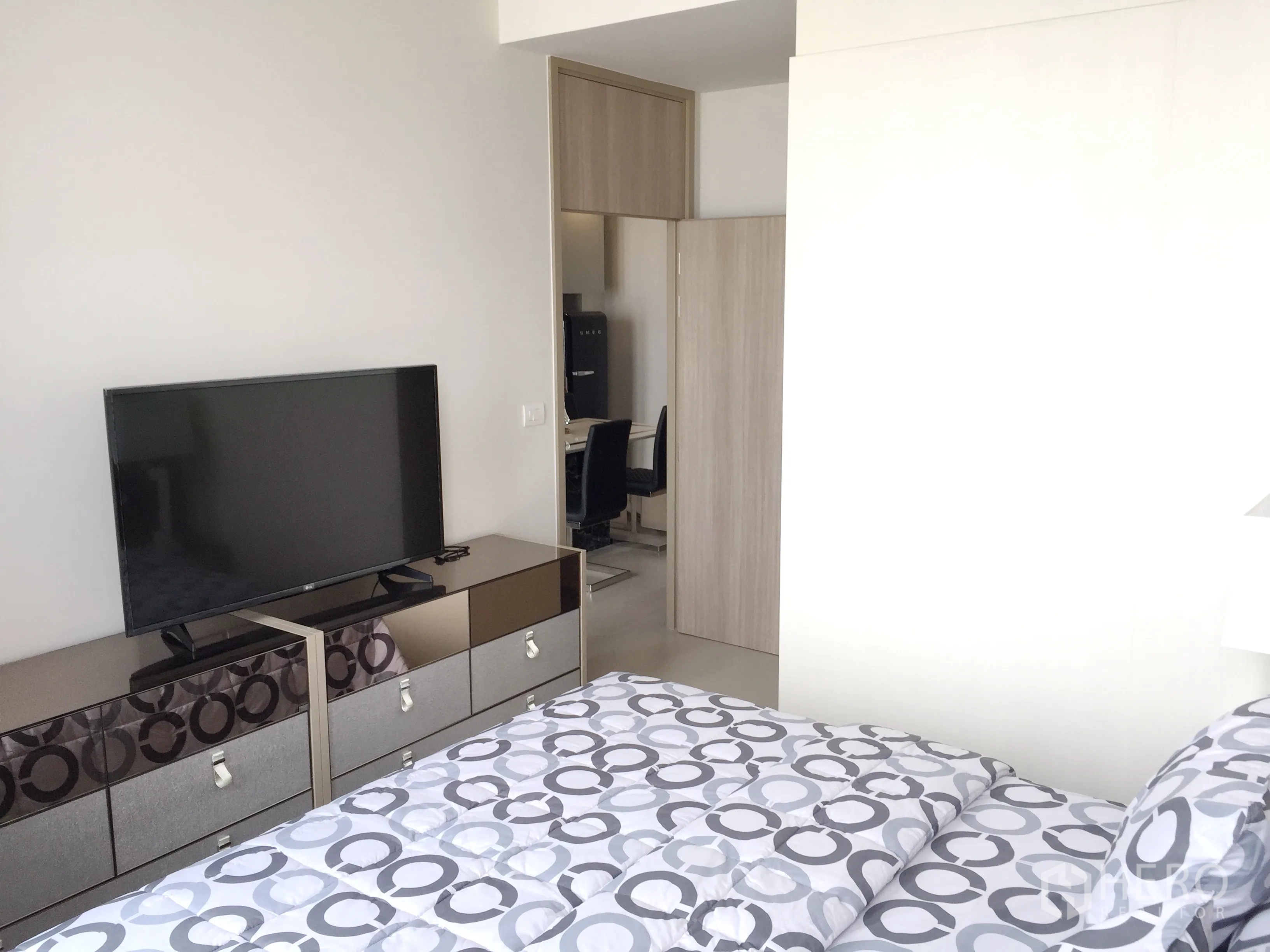 Condominium for rent in Pathum Wan, Bangkok - Bedroom with flat-screen TV on mirrored drawers and doorway to a compact work nook.