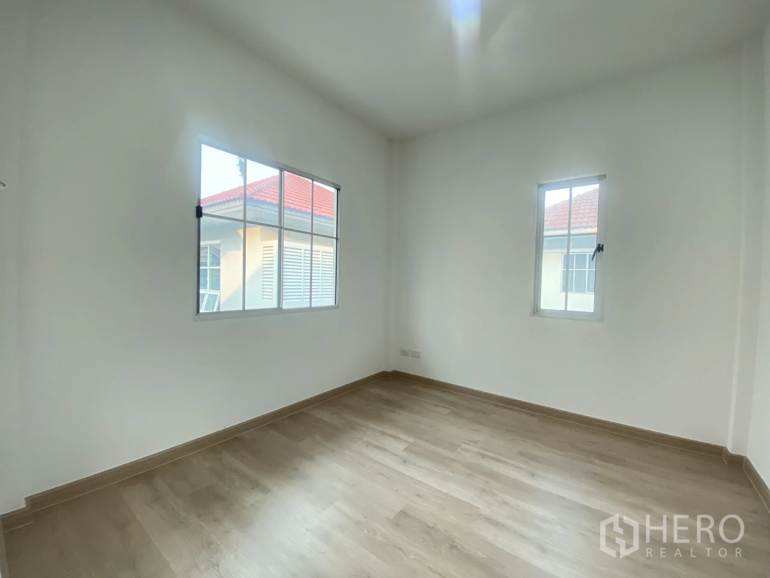 Detached House for sale in Nonthaburi - Sunlit bedroom with two windows and light wood flooring.