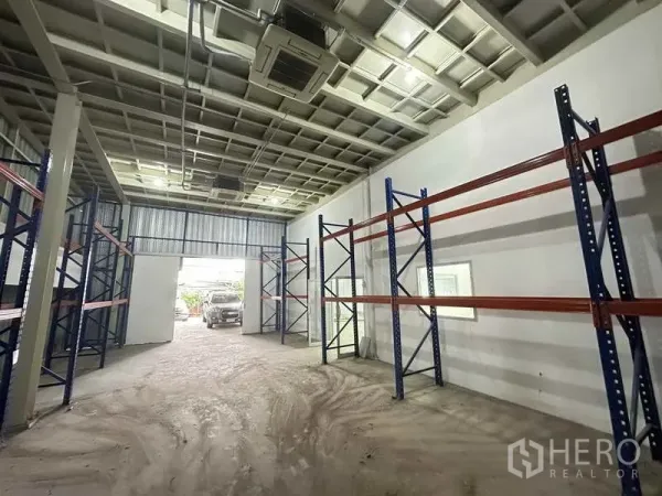 Home Office for rent in Bang Khen, Nonthaburi - Warehouse aisle with pallet racking and a high ceiling, vehicle visible at the wide doorway.