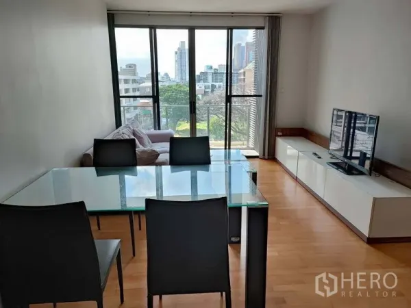 คอนโด ขายในKhlong Toei, Bangkok - ห้องนั่งเล่น–รับประทานอาหาร โต๊ะกระจก โซฟา ตู้ทีวี และประตูกระจกบานเลื่อนสู่ระเบียงวิวเมือง