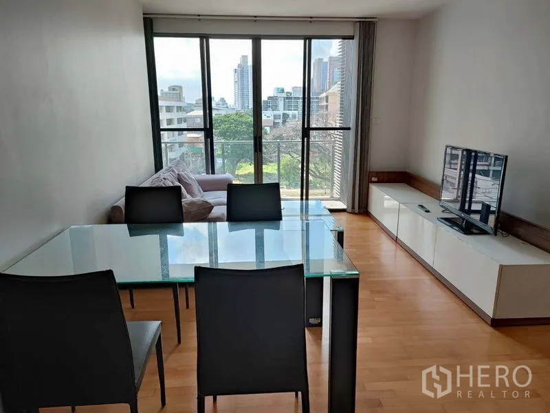 คอนโด ขายในKhlong Toei, Bangkok - ห้องนั่งเล่น–รับประทานอาหาร โต๊ะกระจก โซฟา ตู้ทีวี และประตูกระจกบานเลื่อนสู่ระเบียงวิวเมือง