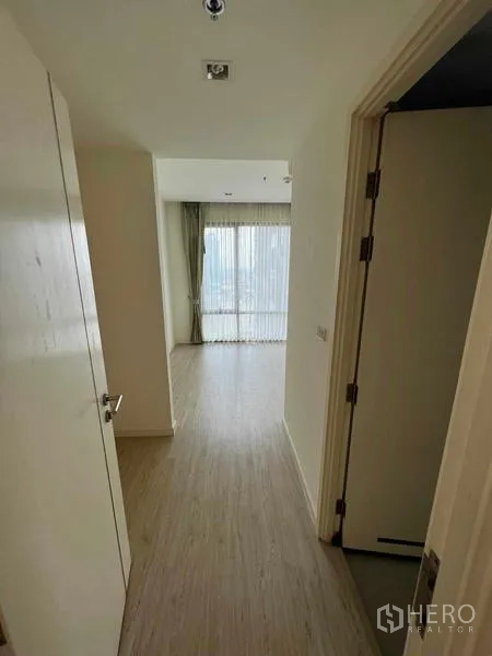 Condominium for sale - Hallway with wood flooring leading to a windowed room with curtains.