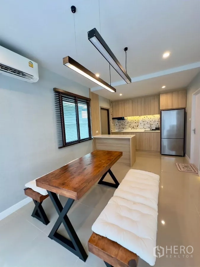Detached House for rent in Samut Prakan - Dining area with wooden table and bench seating, linear pendants, view to kitchen.