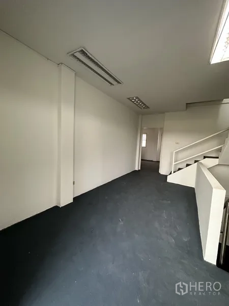 店屋 出租在Bang Na, Bangkok - 楼梯旁办公走廊，日光灯与深色地面。