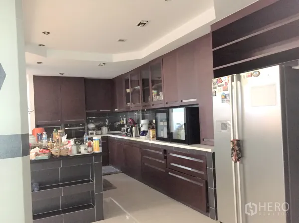 Townhouse for rent in Khlong Toei, Bangkok - Family kitchen with dark wood cabinetry, island counter, built‑in appliances and a stainless refrigerator.
