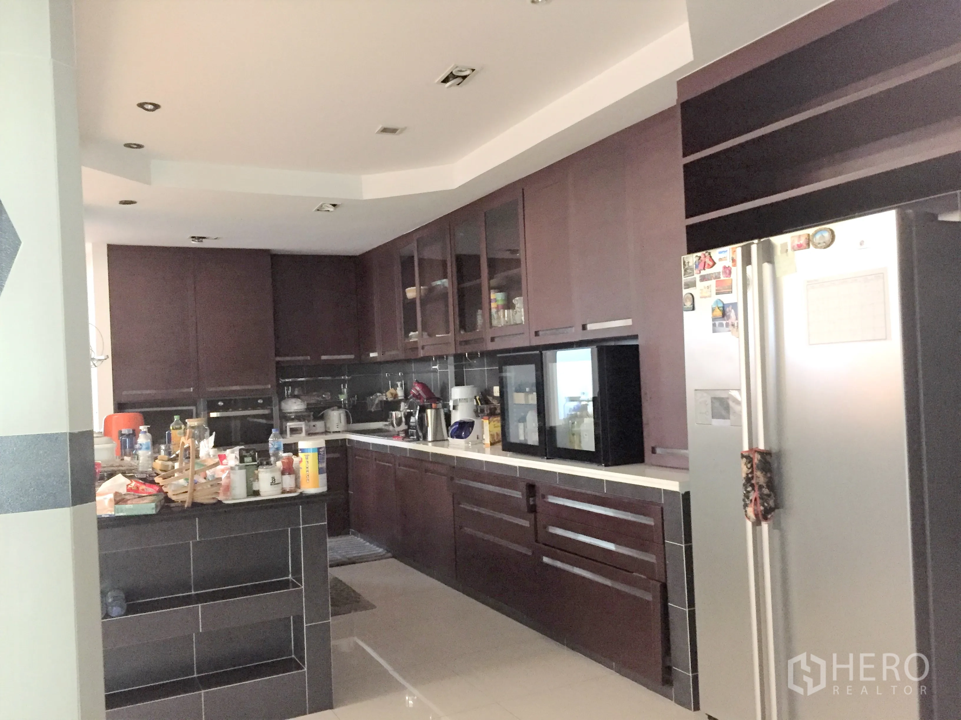 Townhouse for rent in Khlong Toei, Bangkok - Family kitchen with dark wood cabinetry, island counter, built‑in appliances and a stainless refrigerator.