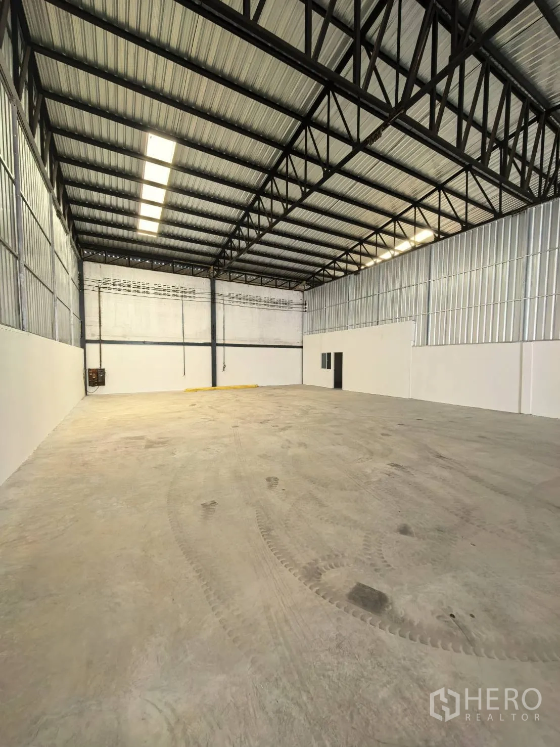 Warehouse for rent in Suan Luang, Bangkok - Open-plan warehouse interior with high roof, lighting strip, and doorway at the end wall.