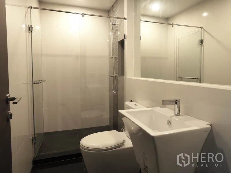Condominium for rent in Sathon, Bangkok - Modern bathroom with glass-enclosed shower, wide mirror, square basin and toilet.