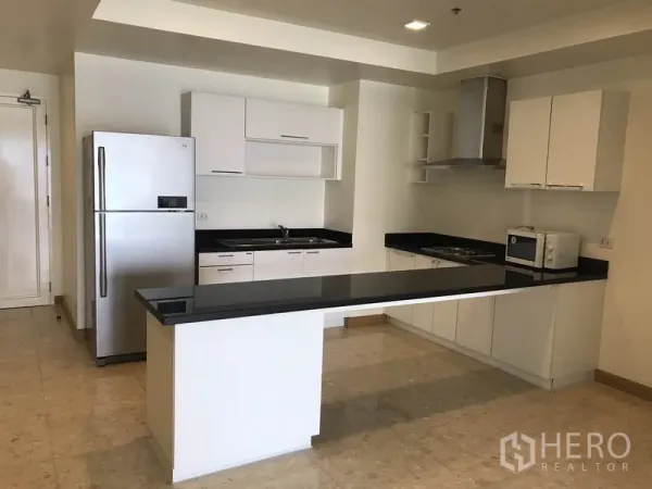 Condominium for rent in Khlong Toei, Bangkok - U-shaped kitchen with white cabinets, stainless refrigerator and extended breakfast island.