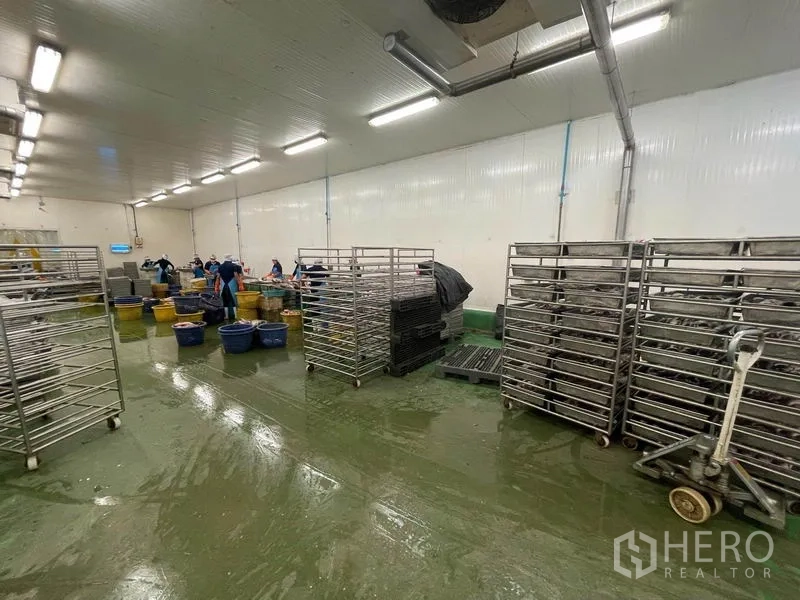 工厂 出售在Mueang Samut Sakhon, Samut Sakhon - 低温加工间，配不锈钢移动货架、塑料桶与绿色环氧地坪，照明明亮。