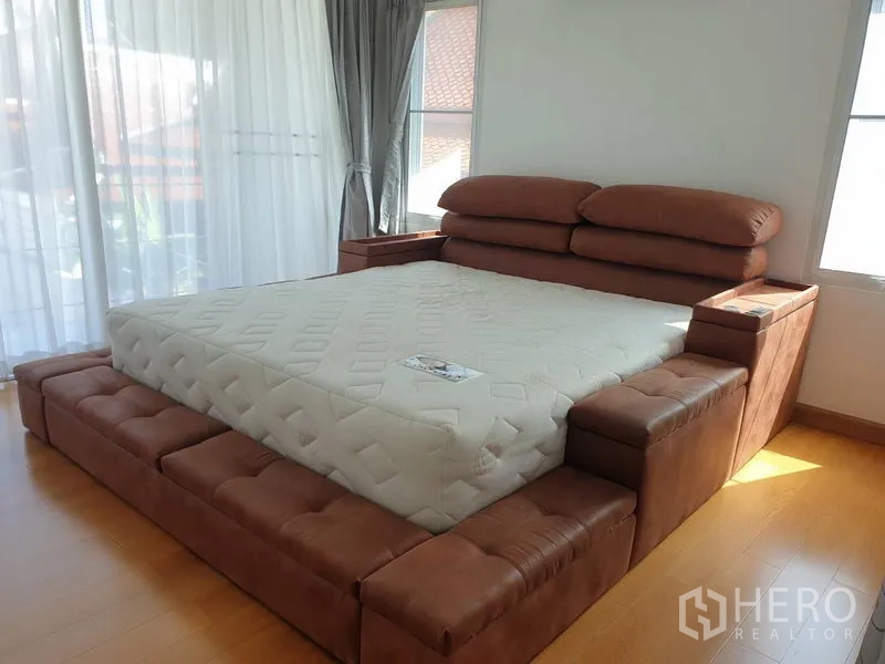 Detached House for rent in Khlong Toei, Bangkok - Spacious corner bedroom with large brown platform bed and wood flooring.