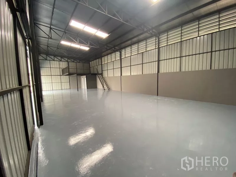 Warehouse for rent in Wang Thonglang, Bangkok - Spacious warehouse interior with high steel truss roof, skylights, epoxy floor and mezzanine with stairs