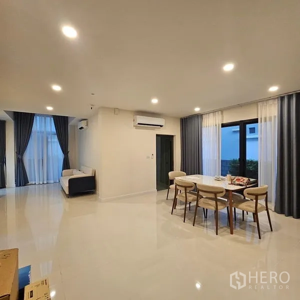 บ้าน ให้เช่าในSaphan Sung, Bangkok - พื้นที่นั่งเล่นและรับประทานอาหารแบบโอเพ่นแปลน หน้าต่างบานใหญ่ ไฟดาวน์ไลท์ และพื้นกระเบื้องเงา.