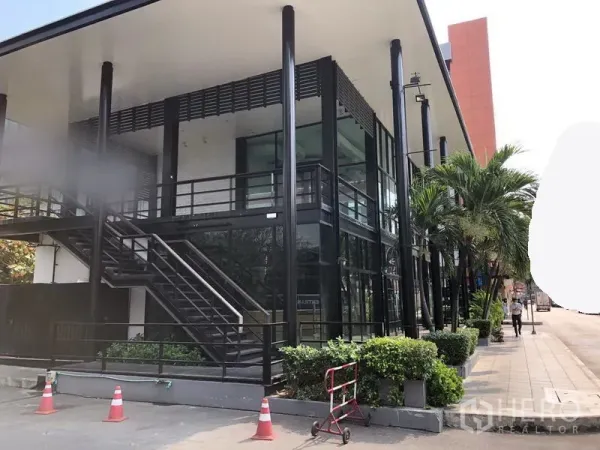 พื้นที่ขายปลีก ให้เช่าในKhlong Toei, Bangkok - มุมมองด้านข้างของอาคารคอมเมอร์เชียล โครงเหล็กสีดำ บันไดภายนอก กระจกบานใหญ่ และต้นไม้ริมทางเดิน