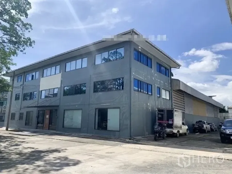 Warehouse for rent in Saphan Sung, Bangkok - Three-storey office building attached to a warehouse with parking and loading area under a clear sky.
