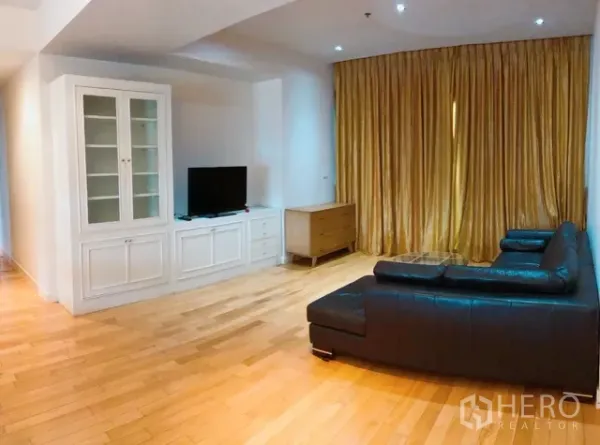 Condominium for rent or sale in Khlong Toei, Bangkok - Cozy lounge with gold drapes, white built-in cabinetry, flat-screen TV and leather sofa on light wood flooring.