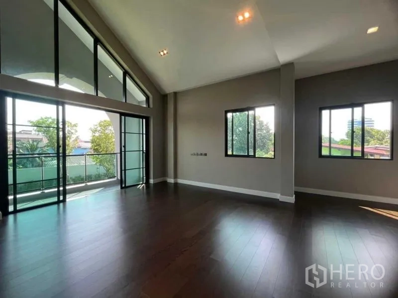 Detached House for sale in Mueang Nonthaburi, Nonthaburi - Upper-level bedroom with vaulted ceiling, dark wood floors, and balcony windows.