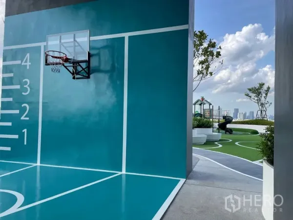 Condominium for rent or sale in Bangkok - Rooftop multi-purpose court with a wall-mounted basketball hoop beside landscaped sky garden and city skyline.