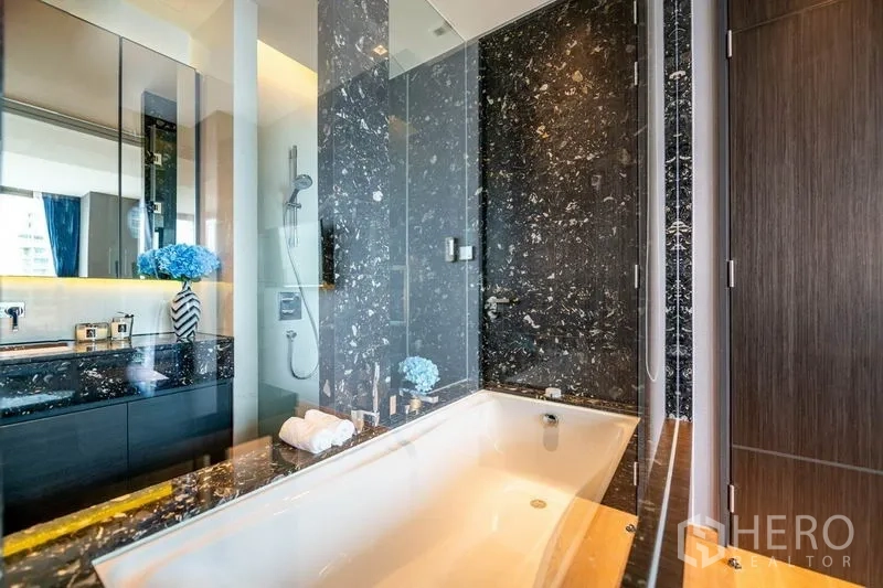Condominium for rent or sale in Khlong Toei, Bangkok - Marble bathroom featuring a soaking tub beside a glass shower and vanity.