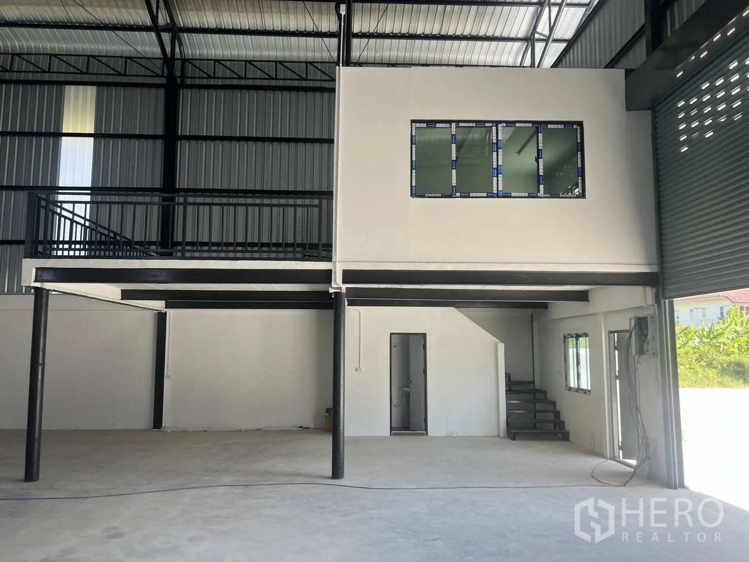 Warehouse for rent in Bang Phli, Samut Prakan - Close view of mezzanine office with windows, stair access, and large roller shutter entrance beside it.