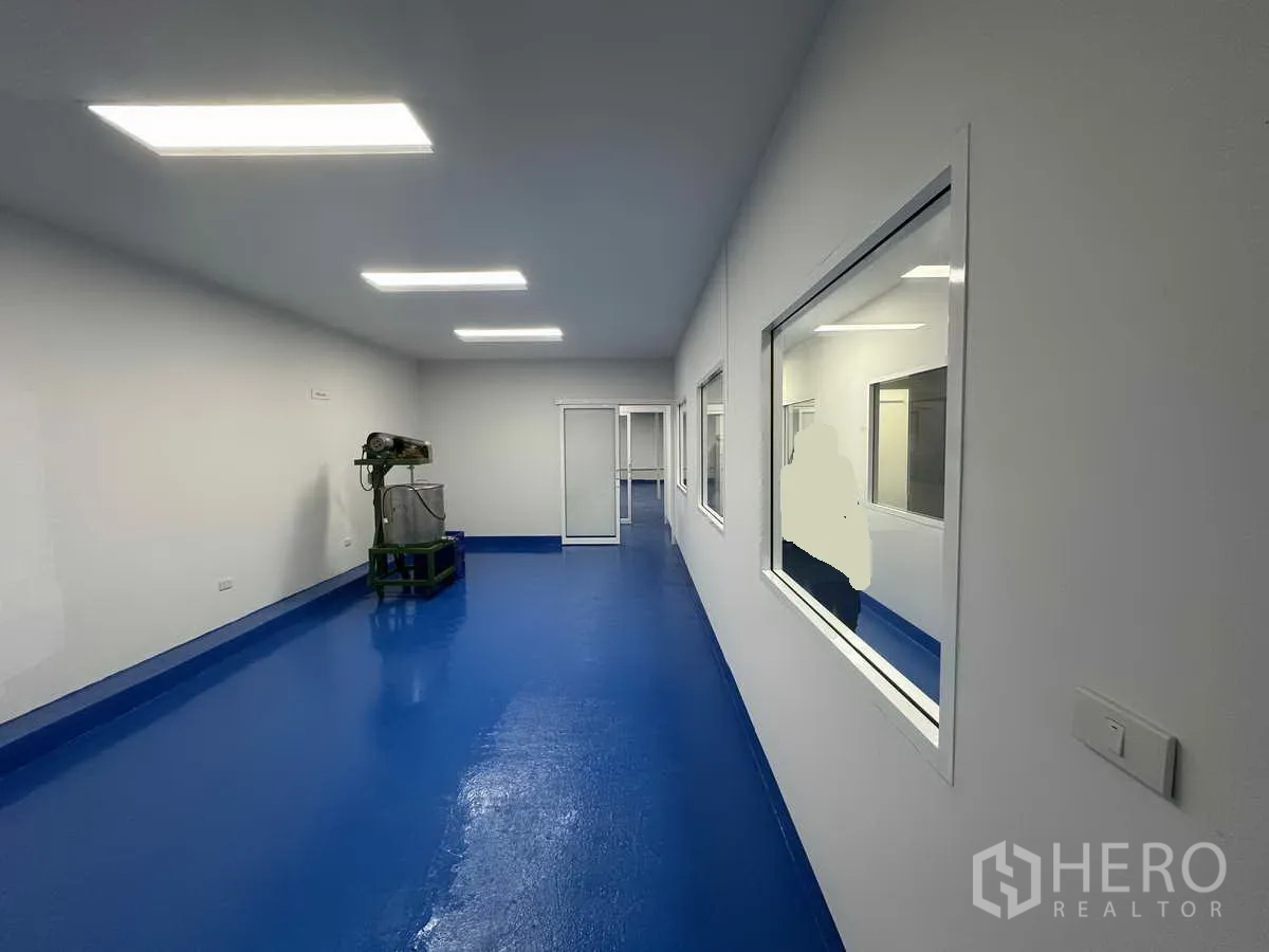 Warehouse for rent in Pak Kret, Nonthaburi - Elongated processing room with viewing windows and sanitary blue floor.