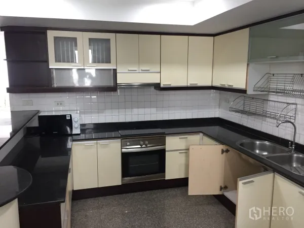 Condominium for rent in Watthana, Bangkok - U-shaped kitchen with granite countertops, double sink, built-in oven, microwave, and ample storage.
