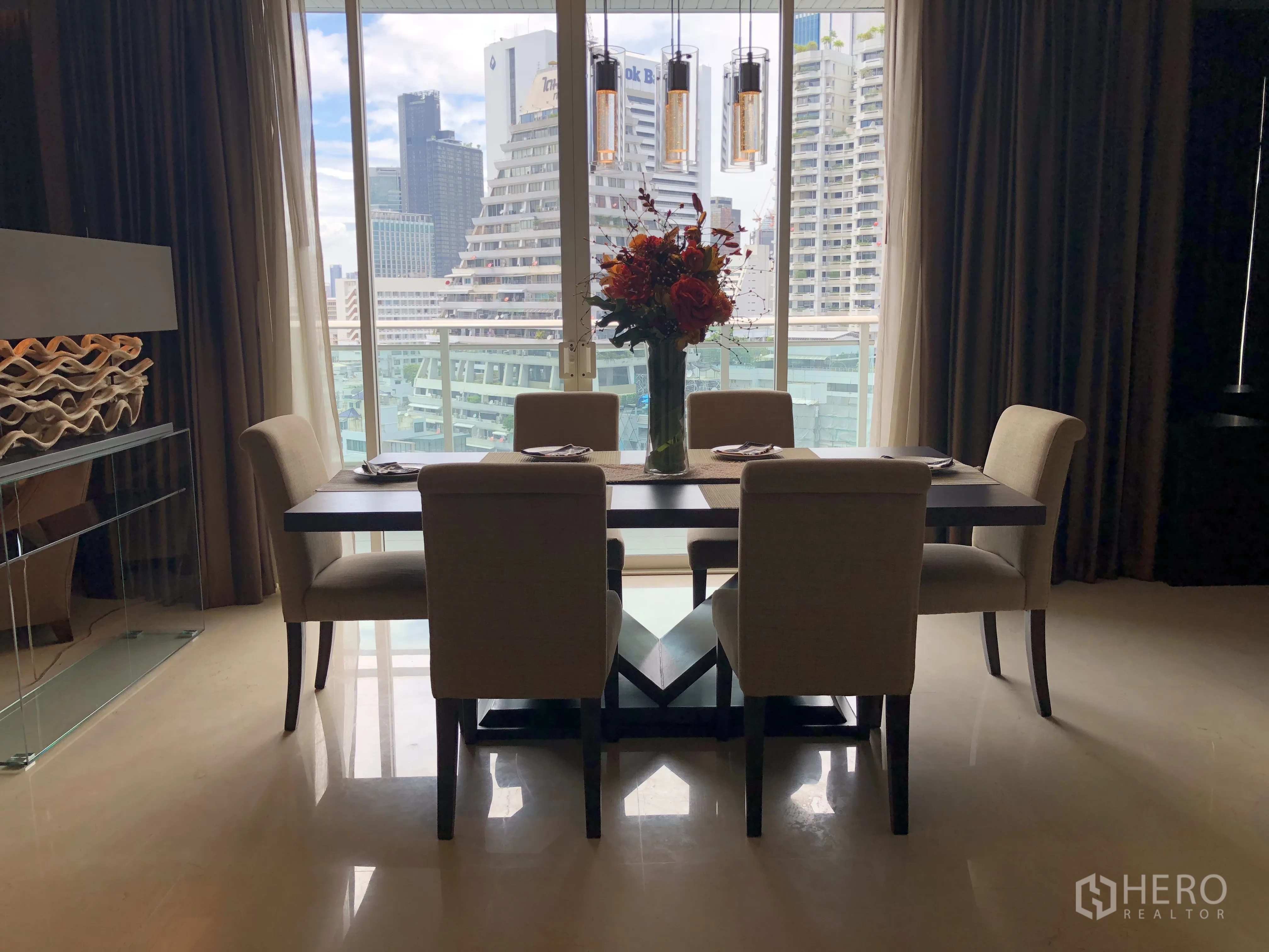 Condominium for rent in Bang Rak, Bangkok - Dining area for six with pendant lights and a large window showcasing the city skyline.