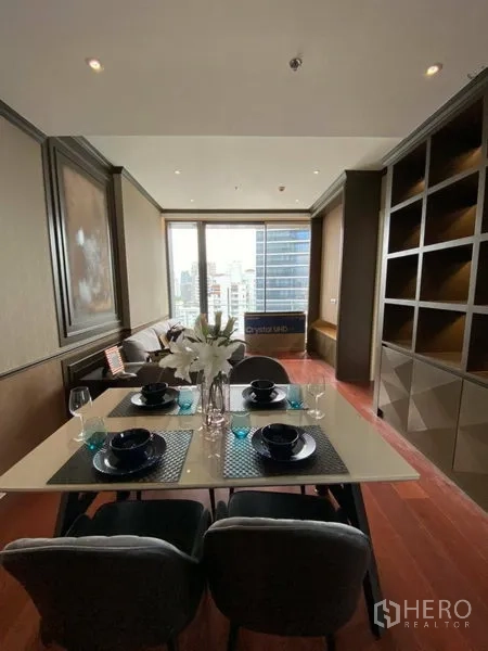 Condominium for rent in Watthana, Bangkok - Dining table for four beside large window with city views and a wall of custom shelving.