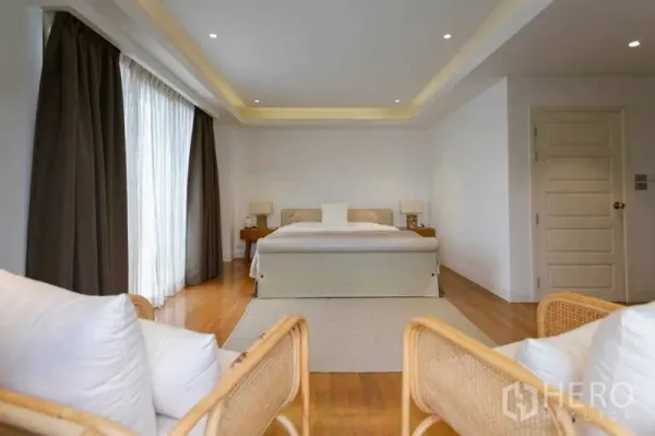 Home Office for sale in Watthana, Bangkok - Spacious bedroom with king bed, wood floors and full-height curtains allowing natural light.