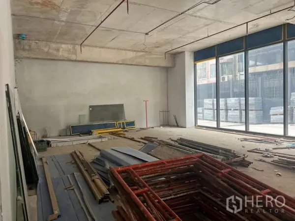 零售空间 出租 - 一层临街毛坯商铺，混凝土高挑天花与整面落地窗，室内堆放施工材料