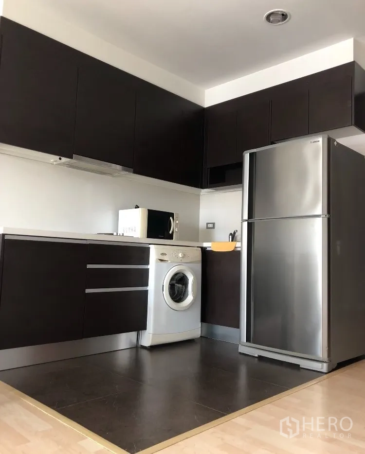 公寓 出租在Watthana, Bangkok - 现代L型厨房，深色橱柜、冰箱、微波炉和洗衣机。