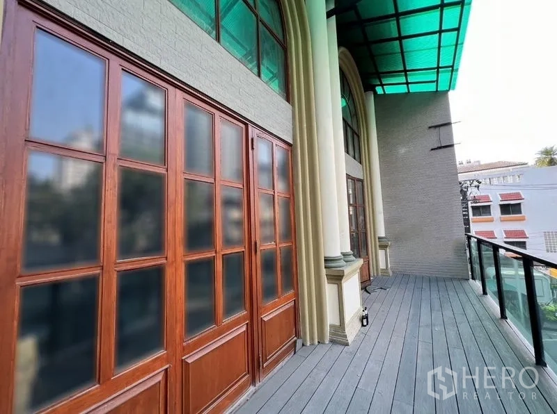 อาคารพาณิชย์ ให้เช่าในWatthana, Bangkok - ระเบียงชั้นบนของอาคารพาณิชย์สุทธิพุ่มวิทย์ พร้อมราวกระจก เสาโค้ง และประตูไม้ ใต้หลังคาเขียวใส.