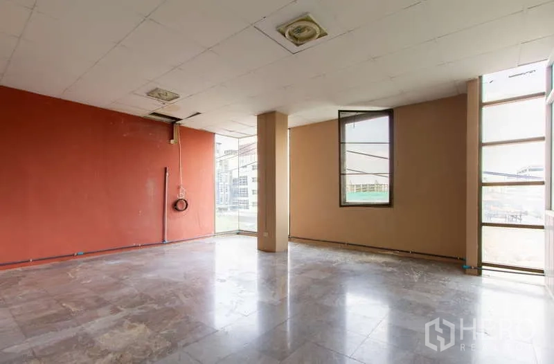 办公空间 出租或出售在Huai Khwang, Bangkok - 采光良好房间，红色强调墙、立柱与大窗城市景观。