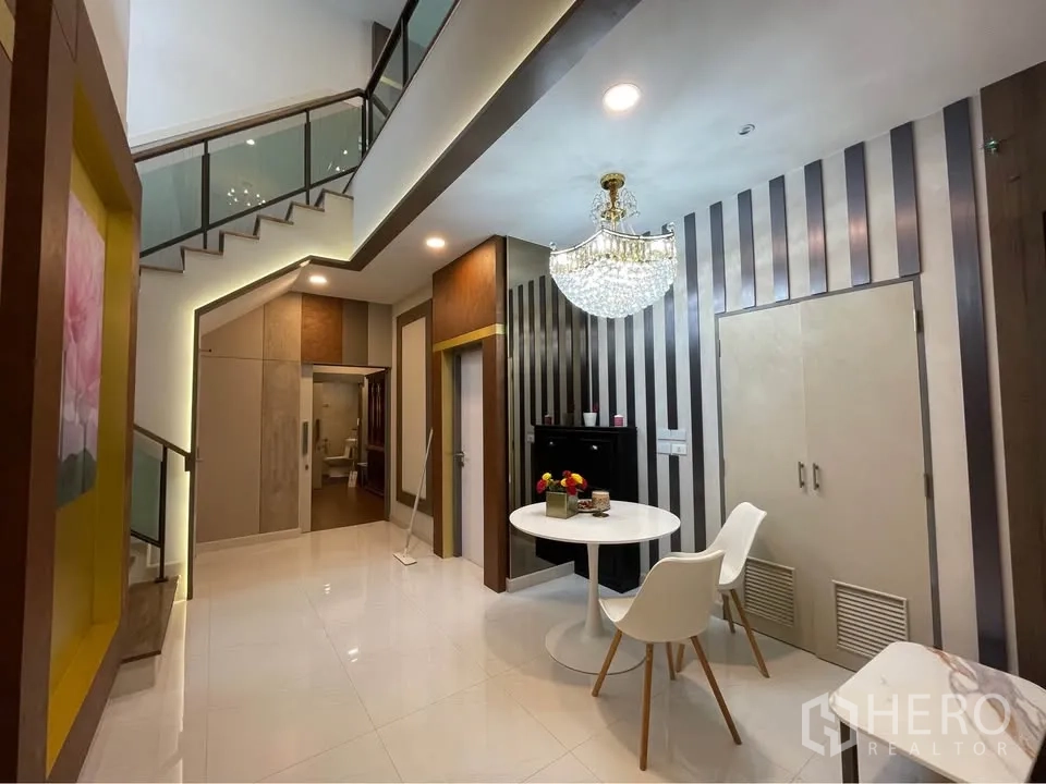 บ้านเดี่ยว for rent or sale in Bang Phli, Samut Prakan - ชานพักบันไดผนังลายทางพร้อมโคมแชนเดอเลียร์และมุมนั่งเล่นเล็ก