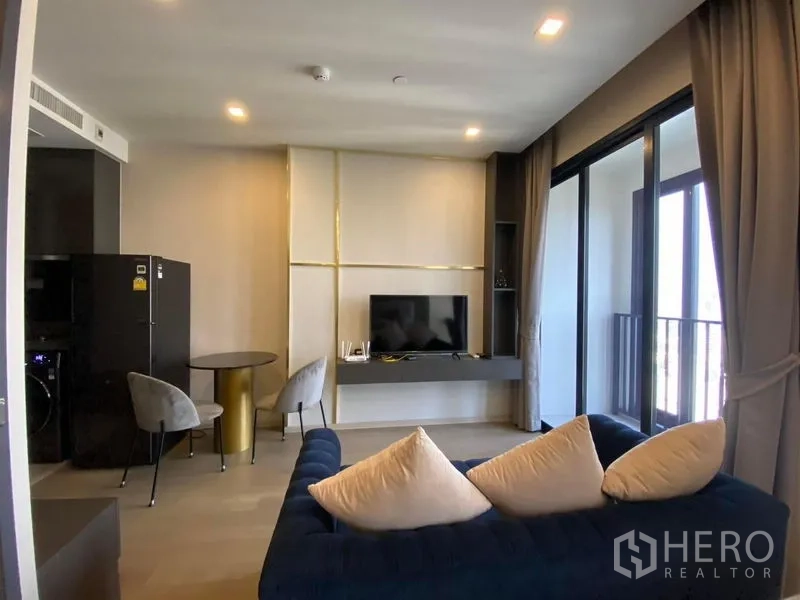 Condominium for rent in Watthana, Bangkok - Living area with TV wall, blue sofa, and balcony access.