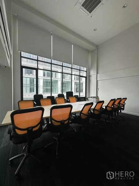 Home Office for rent - High-ceiling boardroom with a long table, orange task chairs and floor-to-ceiling windows.