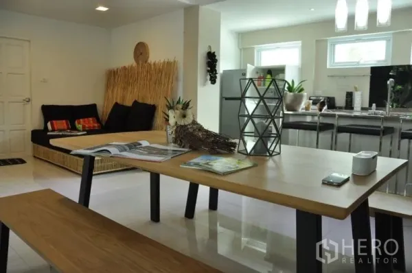 Townhouse for rent or sale in Watthana, Bangkok - Open-plan living and dining area with wooden table, sofa seating and a view to the modern kitchen.