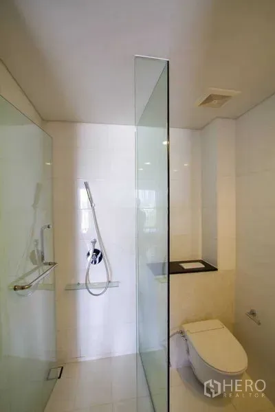 คอนโด ให้เช่าหรือขายในWatthana, Bangkok - ห้องน้ำสมัยใหม่พร้อมพื้นที่อาบน้ำกระจก ฝักบัวแบบมือถือ และโถสุขภัณฑ์ติดผนัง ผนังกระเบื้องสีขาว