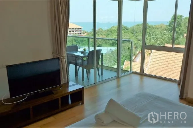 Condominium for sale in Bang Lamung, Chon Buri - Bedroom with TV and sliding glass doors to a balcony overlooking treetops and the sea.