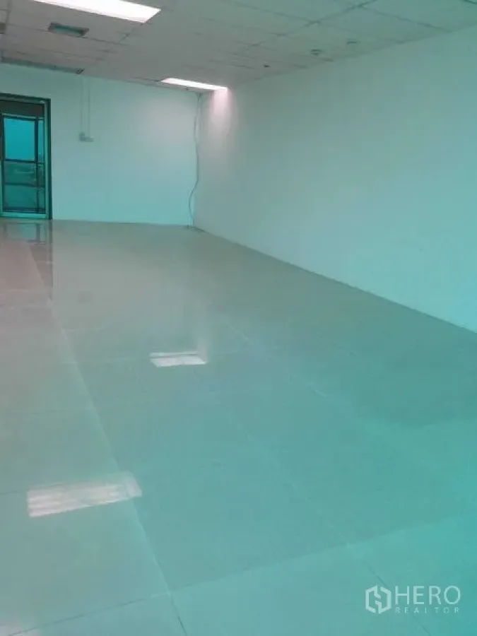 Office Space for rent in Huai Khwang, Bangkok - Long open-plan office with white walls, tiled floor, suspended ceiling, and rear doorway.