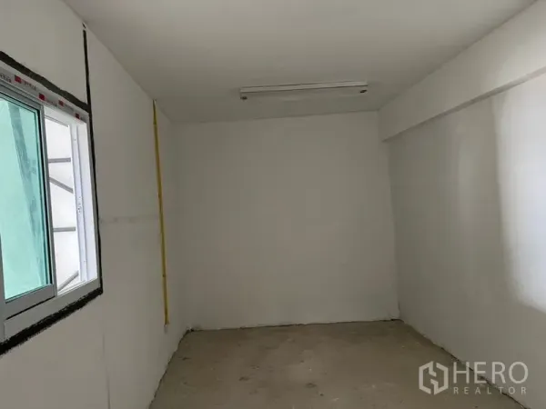 Warehouse for rent in Suan Luang, Bangkok - Compact office room inside the warehouse with sliding window, white walls, and ceiling light.