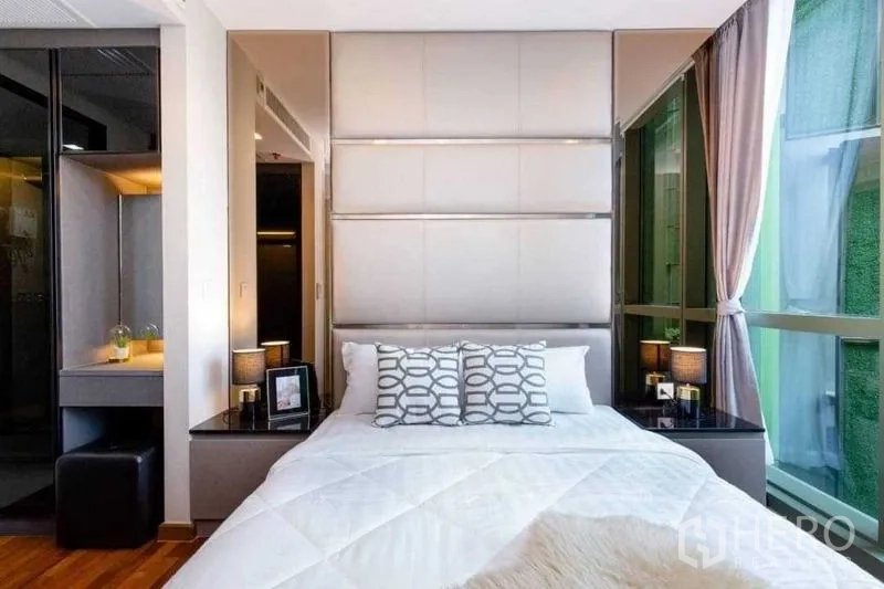 Condominium for sale in Ratchathewi, Bangkok - Bedroom with tall upholstered headboard, corner windows, and a dressing nook.
