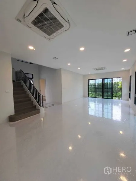 Detached House for rent in Saphan Sung, Bangkok - Open-plan living area with high ceiling, staircase, and full-height sliding doors to the garden.