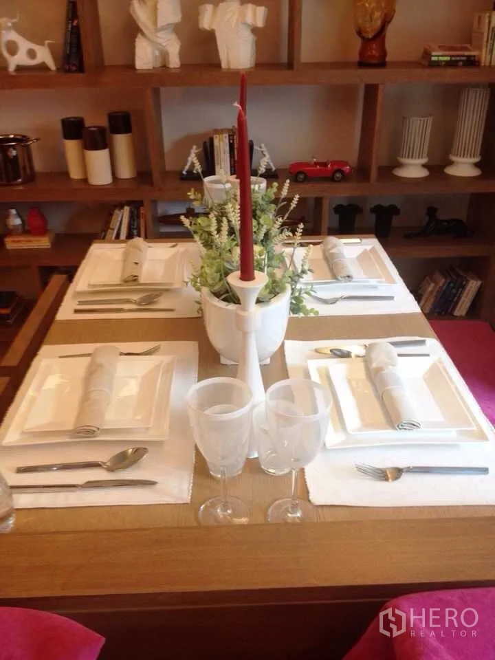 คอนโด ให้เช่าในWatthana, Bangkok - โต๊ะอาหารจัดสำหรับสี่ที่ พร้อมเครื่องใช้สีขาวและเทียนสีแดง มีชั้นไม้ตกแต่งด้านหลัง