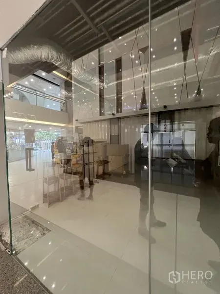 零售空间 出租 - 近距离拍摄的落地玻璃立面，可见室内灯光与中庭环境。