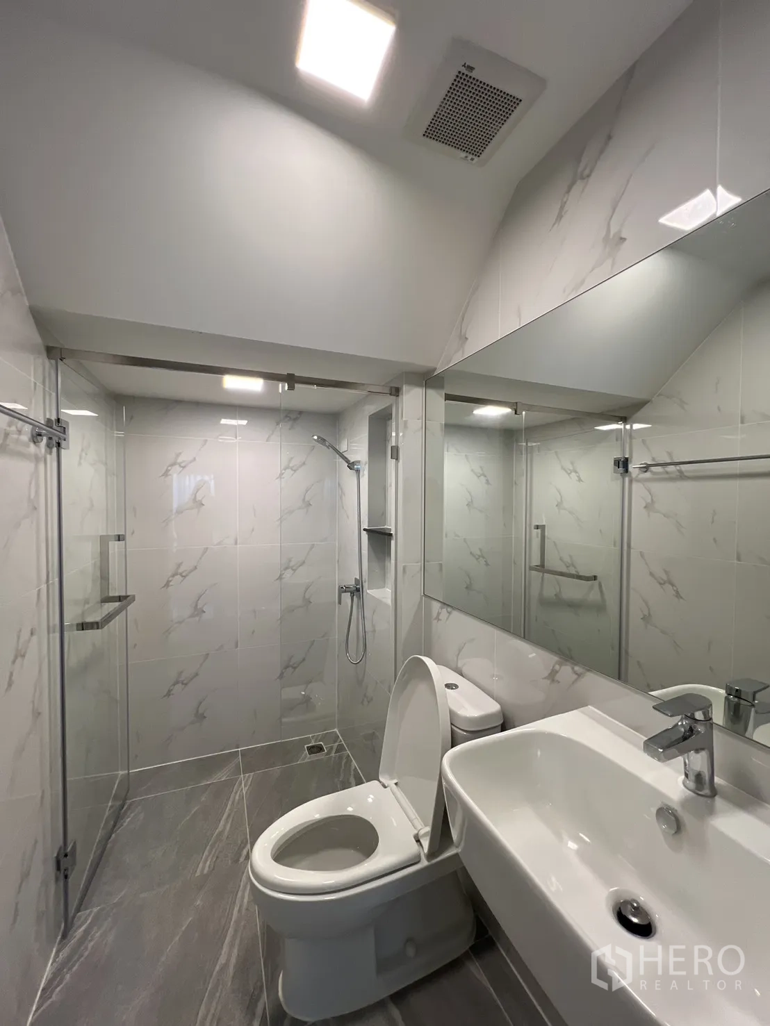 Detached House for rent in Prawet, Bangkok - Guest bathroom with glass shower, vanity and marble-style tiles.