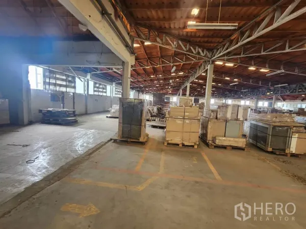 工厂 出租在Mueang Samut Sakhon, Samut Sakhon - 宽敞仓库内部，钢梁屋顶，堆放着装箱托盘。